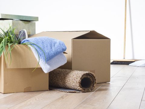 Umzugskartons auf Parkett vor weißer Wand mit Werkzeug und Besen