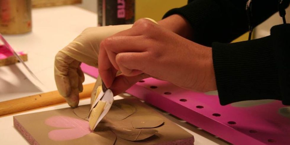 Nahaufnahme einer Hand, die eine gold übermalte Blumen-Schablone von einer rosa bemalten Holzplatte zieht 