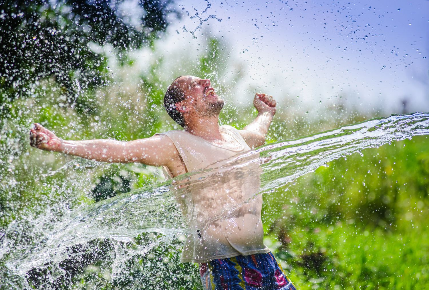 Mann im sommerlichen Garten wird mit Wasser bespritzt