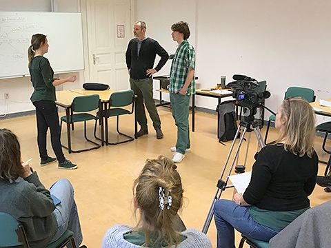 Rhetorikkurs - zwei Männer und eine Frau in einem Rollenspiel. Im Vordergrund die Kursleiterin mit Videokamera.