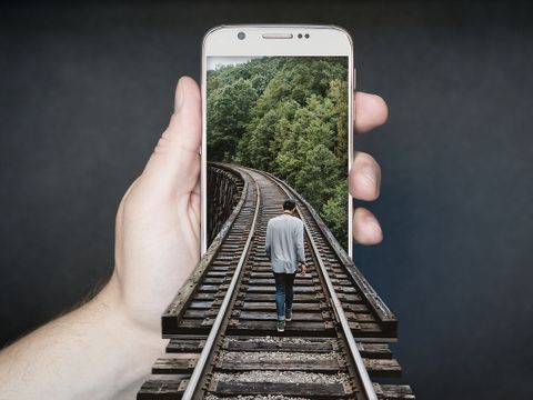 Ein Mann folgt Bahnschienen direkt in eine Smartphone - der Weg führt in die digitale Zukunft.