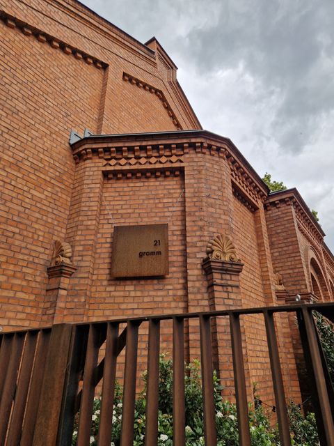 Backsteingebäude mit Verziehrung und 21 gramm Schild hinter einem rostigen Zaun