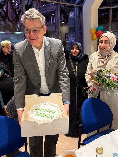 Ramadan Iftar Essen - ein Mann hält einen weißen Karton in der Hand mit einer weißen Sahnetorte mit der Aufschrift "Ramadan Kareem", hinter ihm sind zwei lächelnde Frauen