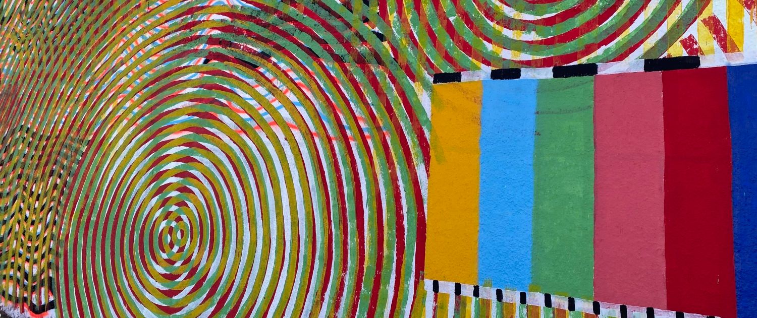 Auf der rechten Bildseite sind mehrere gemalte dicke Streifen nebeneinander. Von Innen nach Außen sieht man folgende Farben: gelb, hellblau, hellgrün, rosa, rot und dunkelblau. Oberhalb noch einmal ein dünner Streifen abwechselnd in weiß und schwarz, der die bunten Balken abschließt. Die weißen und schwarzen Streifen sind schmaler als die bunten streifen darunter. Daneben und darüber viele ineinander gestapelte Kreise, die quasi eine Spirale bilden. Jeder einzelne Kreis ist grün und ist noch einmal mit roter Farbe nachgefahren. Dazwischen sind weiße, schmale Leerräume. Es handelt sich bei diesem Bild um ein gemaltes Kunstwerk