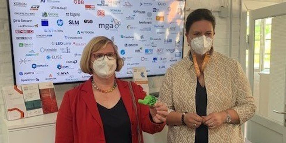 Zwei Frauen, eine hält etwas 3D-gedrucktes in die Kamera.