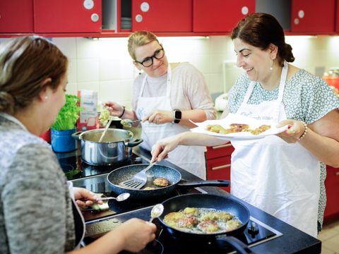 Drei Frauen stehen um eine Kochinsel und kochen gemeinsam