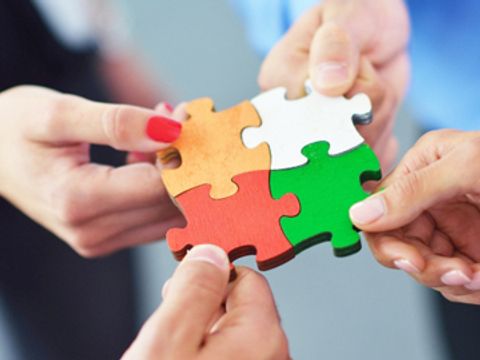 vier Hände stecken Puzzleteile zusammen