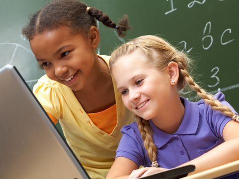 zwei Kinder vor einem Laptop mit Tafel im Hintergrund