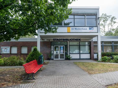 Ein Haus mit der Aufschrift „Stadtbibliothek“, davor eine rote Bank