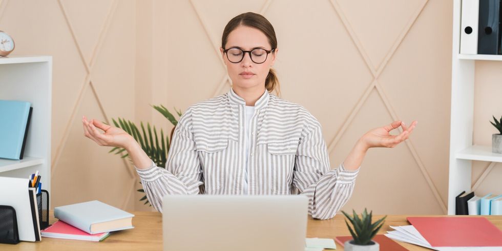 Businesswoman meditating yoga practice on workplace after hard day, deadline concept. Stress relief
