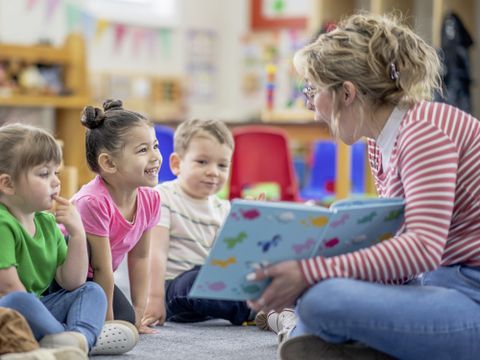 Ausbildung Erzieherberuf - Vier Kinder sitzen vor einer Erzieherin, die ein aufgeschlagenes Buch zeigt
