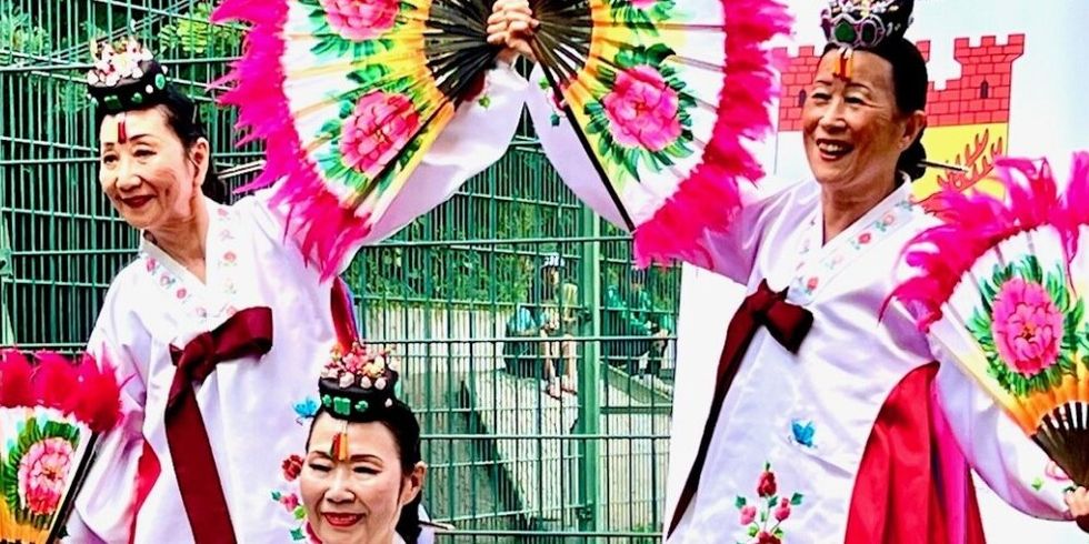 Drei buntgekleidete asiatische Frauen tanzen mit großen Fächern.