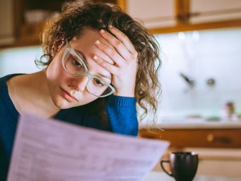 eine Frau liest eine Rechnung und hat den Kopf auf die Hand gestützt, sie macht einen besorgten Eindruck