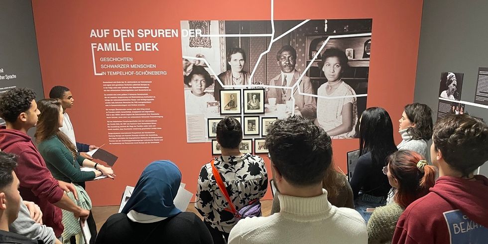 Menschen stehen vor einer Tafel mit Fotos mit dem Text: Auf den Spuren der Familie Dieck