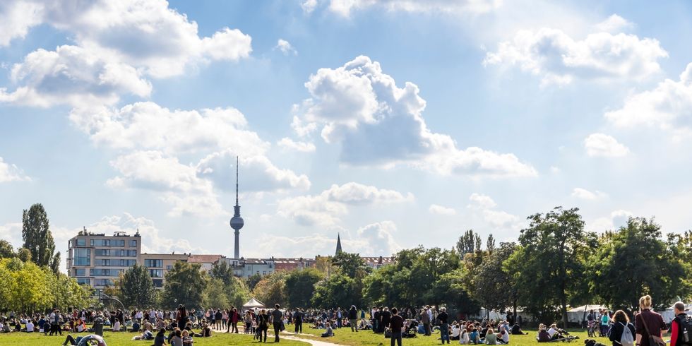 Berliner Mauerpark mit vielen Menschen, die in Gruppen sitzen oder stehen, im Hintergrund der Fernsehturm und Gebäude