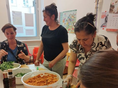 Vier Frauen sitzen und stehen an einem Tisch, sie bereiten einen Bulgursalat vor