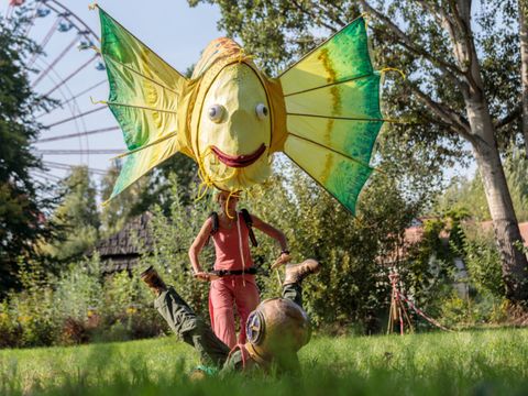 Fotografie einer Theaterinszenierung im Freien mit einem großen Fischkostüm.