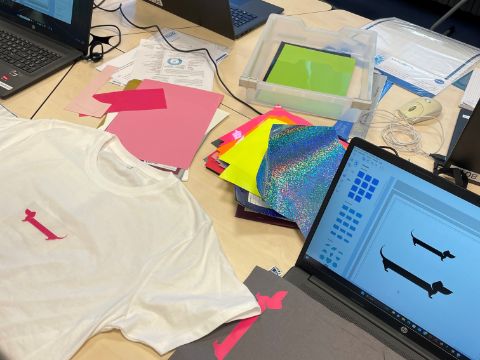 Tisch mit Laptops, verschiednenen Materialien zum Plotten und ein T-Shirt
