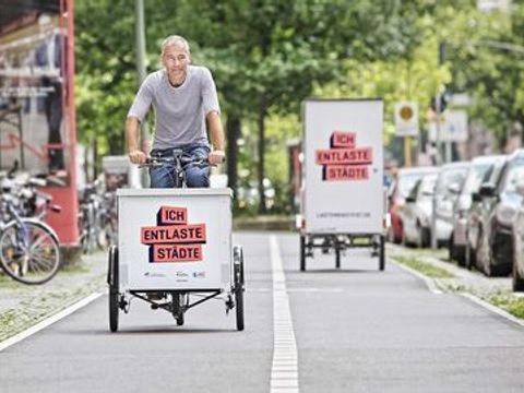 In zwei Richtungen geteilter Fahrradweg zwiachen Füßgängerbereich und parkenden Autos. In beiden Richtungen fahren Lastenräder mit der Aufschrift ich entlaste Städte.