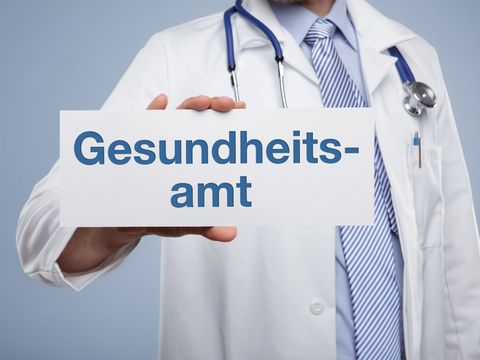 Arzt hält Schild mit der Aufschrift "Gesundheitsamt"