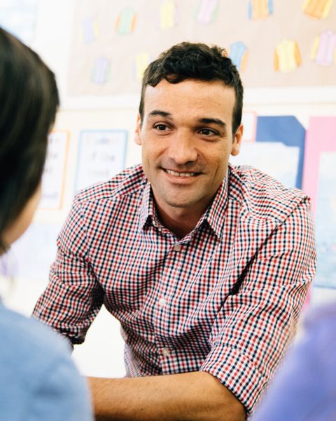 Ein Lehrer sitzt drei Schülerinnen gegenüber und spricht
