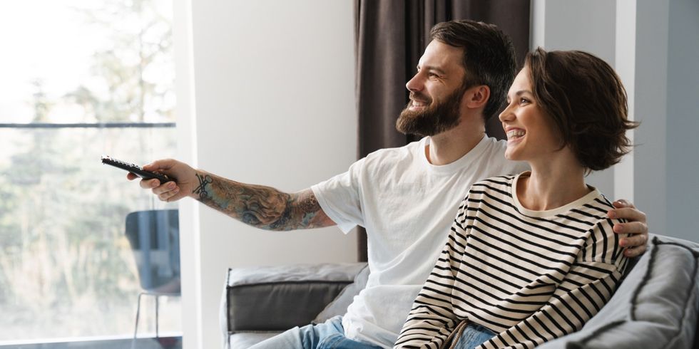 glückliches weißes Paar schaut TV und sitzt auf einer Couch