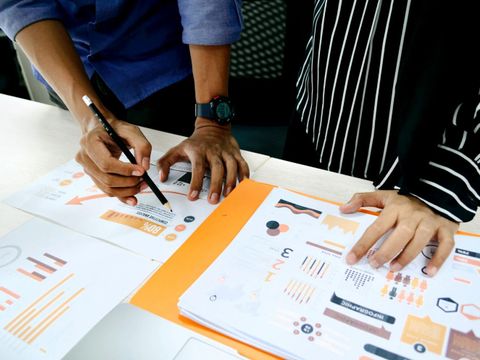 Zwei Personen haben Datensätze auf dem Schreibtisch ausgebreitet und werten diese zusammen aus.
