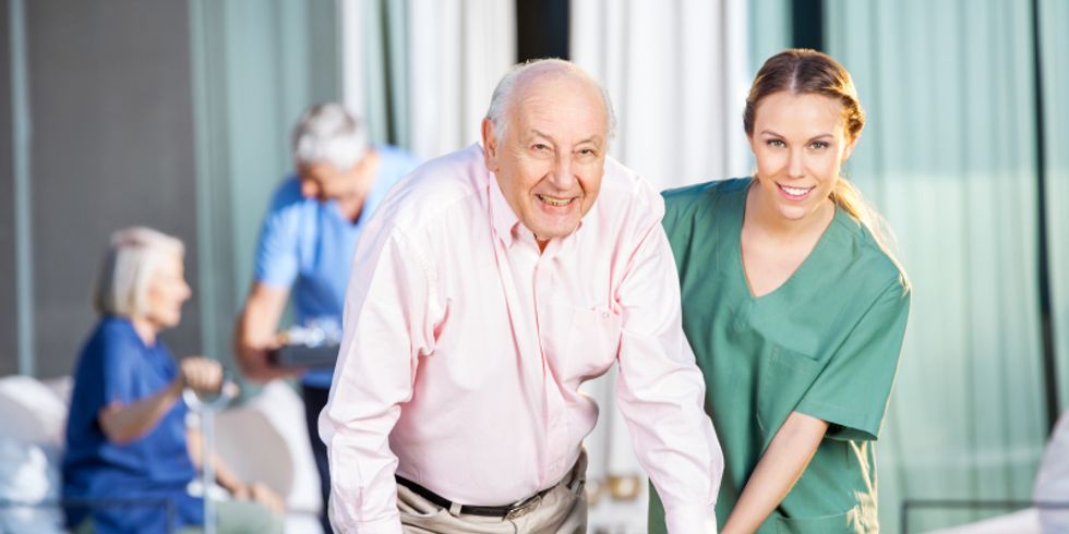Eine junge Pflegerin hilft einem ältern Herren am Gehgestell