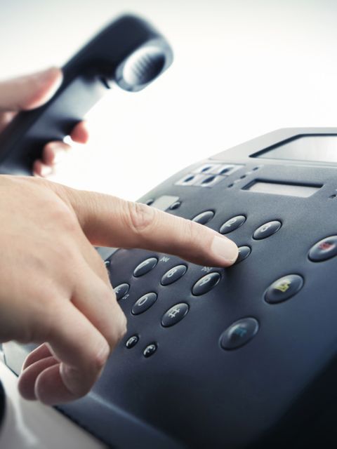 Eine Hand wählt eine Rufnummer auf dem Telefon