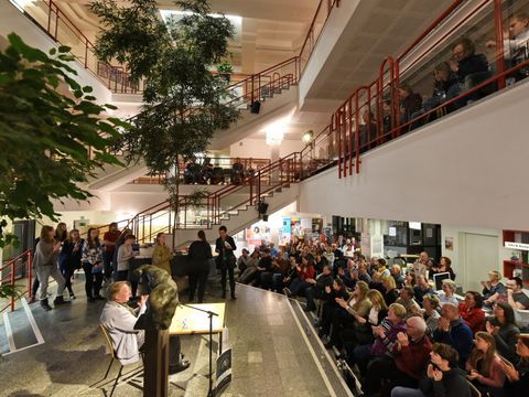 Bühne mit Akteuren und Publikum in mehreren Stuhlreihen