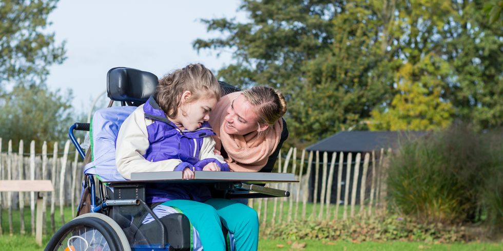 eine Frau beugt sich herunter zu einem Mädchen im Rollstuhl