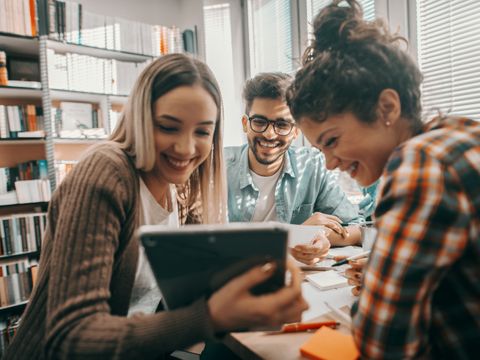 Eine Gruppe Studierender schaut auf ein Tablet und lacht