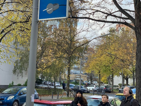 Menschen schauen auf ein Symbol auf einem Schild. Eine Person hat dabei ein Mikrofon in der Hand und eine andere Kopfhörer. Copyright: Fabian Eckert