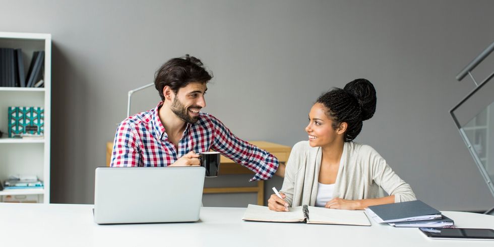 Zwei Personen sprechen am Schreibtisch und machen digitale und analoge Notizen.