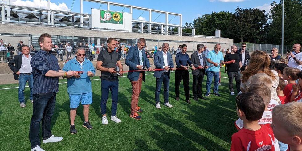 Mehrere Personen stehen auf einem Kunstrasen und schneiden ein rotes Band durch.