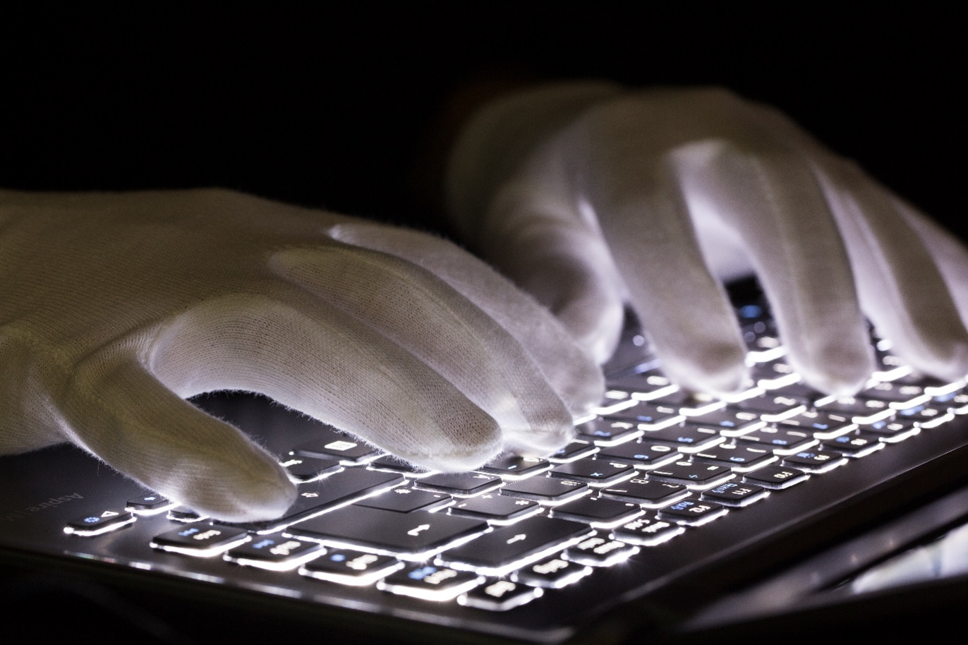 Hände in weißen Handschuhen über einer beleuchteten Tastatur