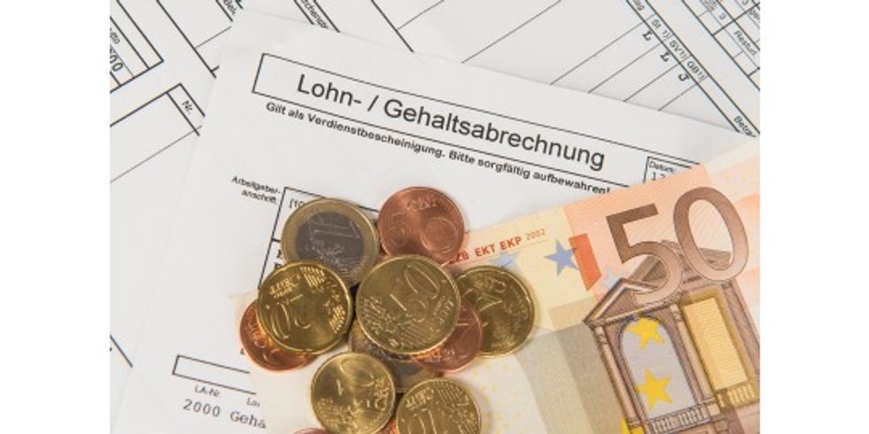 Münzen und Geldscheine liegen auf einer Gehaltsabrechnung