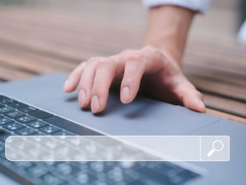 Eine menschliche Hand bedient das Touchpad eines Laptops. Dies symbolisiert die Internetrecherche und das Navigieren über eine Suchmaschine.