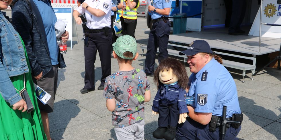 Knieende Polizistin mit einer Puppe vor einem Kind und Eltern