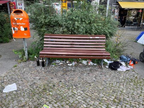 Foto einer Sitzbank, daneben und darunter Müll