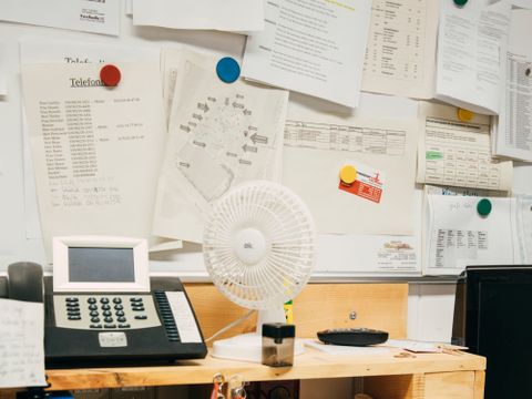 Schreibtisch mit Unterlagen und Telefon vor Pinnwand