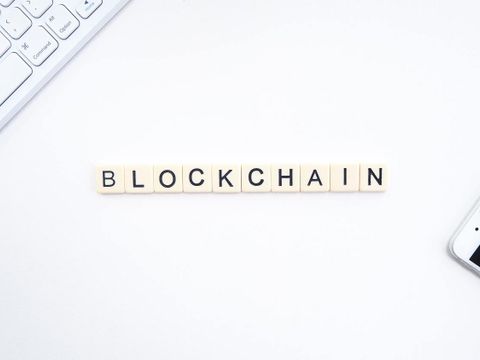 Blockchain buchstabiert mit Computertastatur und Mobiltelefon im Hintergrund
