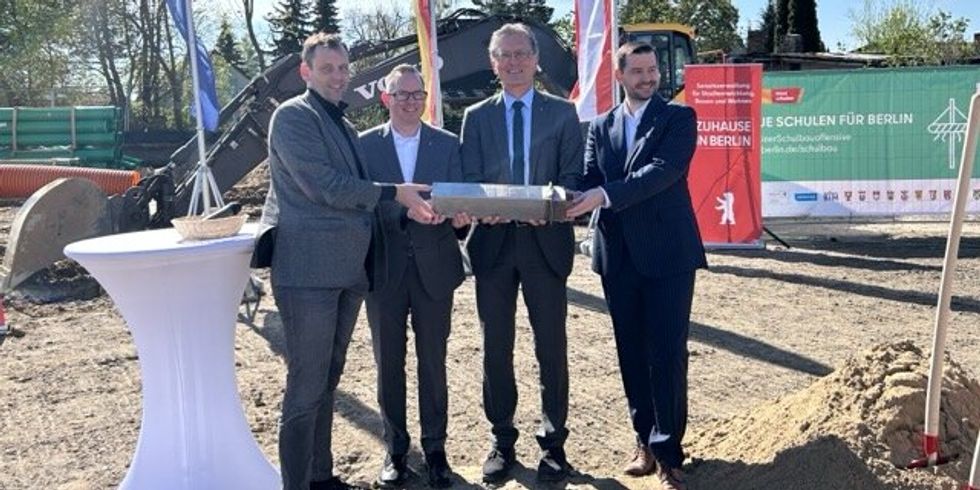 4 Personen auf einer Baustelle, die einen Grundstein gemeinsam halten