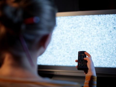 Frau mit Fernbedienung vor einem Fernseher