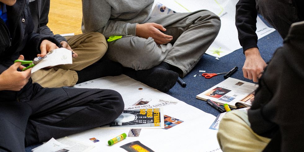 Impressionen von der zweiten Konferenz des 8er-Rates Ende Januar in der Sporthalle Charlottenburg: Jugendliche sitzen mit Scheren, Klebestiften und Papier auf dem Boden und erstellen eine Collage aus Zeitungs- und Bildausschnitten. Aufnahme von den Jugendlichen ohne Gesichter.