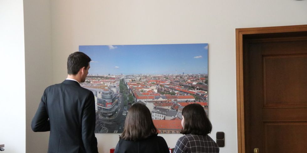 Gemeinsam mit dem Bezirksbürgermeister blicken die beiden Girls-Day-Besucherinnen auf ein Foto Neuköllns.
