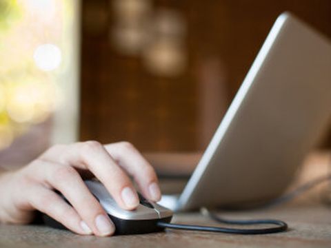 Hand auf der Maus neben einem Laptop