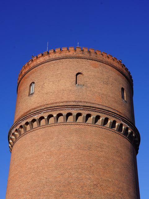 Ziegelstein-Wasserturm mit Rundbogenfries und Zinnen vor blauem Himmel