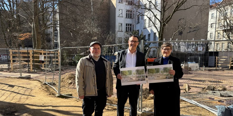 Drei Personen stehen auf einem Baustellengelände, zwei halten Pläne mit Landschaftsbildern