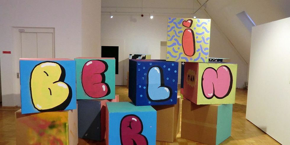 Große Würfel aus Karton sind mit bunten Grafiken bilden einen Stapel, unter anderem sind die Buchstaben "B, E, R L, I, N" zu sehen